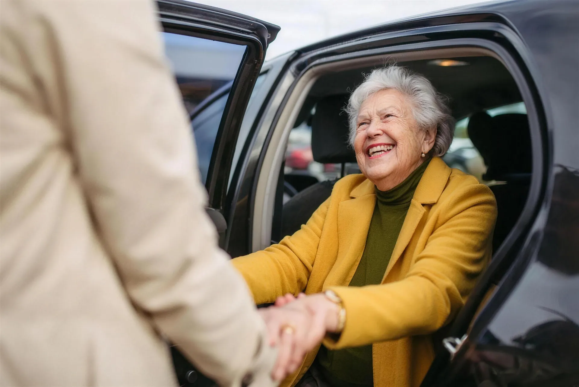A caregiver helping a smiling senior woman out of the car
